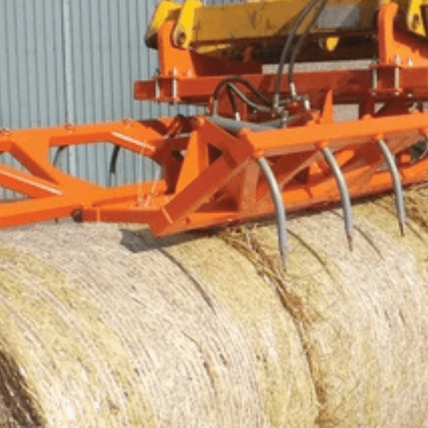 A hay baler in action, loading freshly cut hay bales onto a trailer in a sunny field.